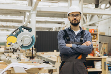 Carpenter wearing hardhat and safety glasses posing with arms crossed in workshop