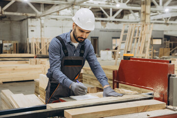 Carpenter taking notes on wooden plank in workshop