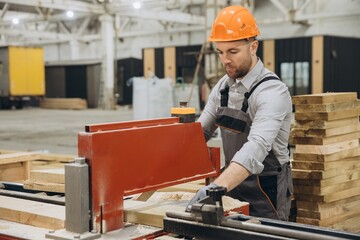 Carpenter working with wood plank and precision saw in workshop for modular building industry