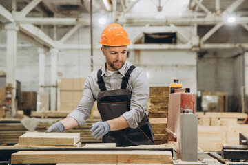 Carpenter working with wood plank and saw in furniture factory