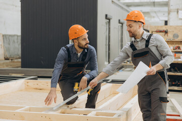 Construction workers measuring wooden frame for modular building
