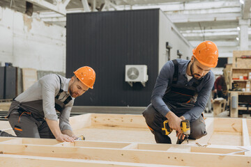 Construction workers building wooden frame for modular house in factory