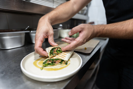 Chef serving grilled chicken spinach tortilla wrap on plate