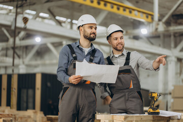 Engineers reading blueprint and discussing project in modular building factory