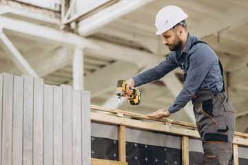 Construction worker building prefabricated modular house using cordless screwdriver