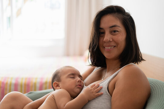 A mother smiles as she holds her sleeping baby on her chest