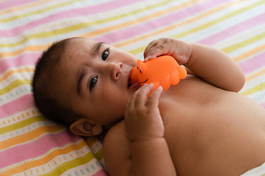Baby biting a toy while lying in bed