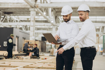 Engineers using laptop are supervising construction of modular building