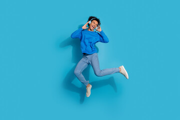Full body photo of attractive young man jump enjoy music dressed stylish clothes isolated on blue color background