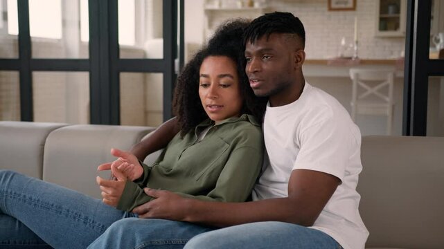 Love couple ethnic family African American man woman husband wife relax together on couch sofa at home casual weekend affectionate girl guy happy male female watching TV bonding hug talk romantic date