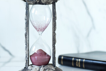 Hourglass and holy bible book on marble table with white background. Copy space. Time countdown,...