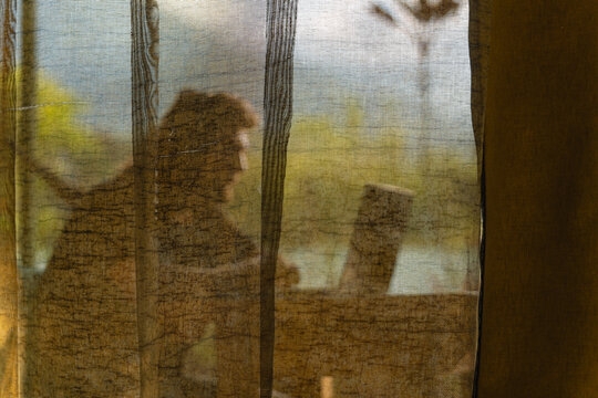 Person behind a curtain working on her computer