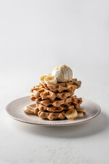 Homemade waffles stack with ice cream, bananas and nuts on white plate isolated on white background, text space