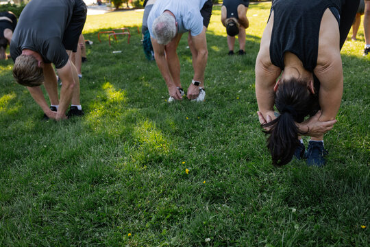 Group of People Stretching Hamstrings Outdoors in a Park on a Su