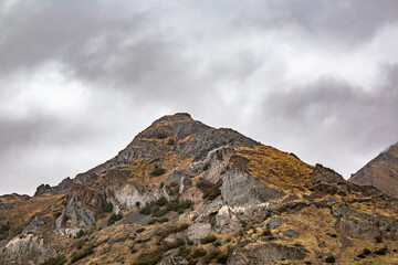 Fototapeta premium A rugged rocky mountain peak with sparse vegetation under a dramatic overcast sky. 