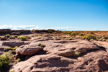 A wide desert landscape featuring red rock formations and scattered desert vegetation under a clear blue sky