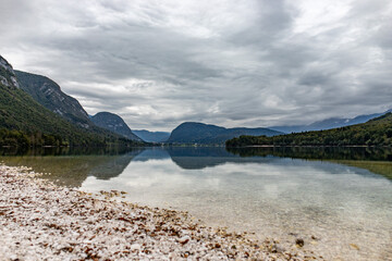 Serene Lake Bohinj in Slovenia, surrounded by lush mountains and reflecting an overcast sky