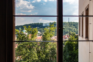 A serene view of Petřín Tower and greenery seen through a Prague Castle window.
