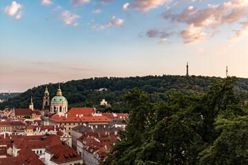 A serene sunset in Prague highlighting red rooftops, St. Nicholas Church, and the iconic Petřín Tower.
