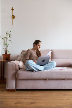 Young woman is sitting on a sofa in her living room, working home