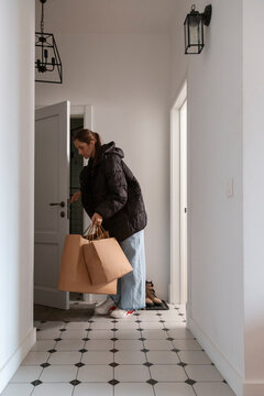 Young woman coming home with shopping bags entering apartment