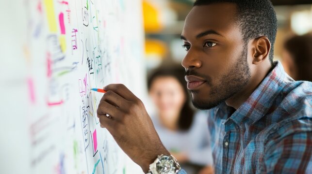 Man adds notes to colorful whiteboard.