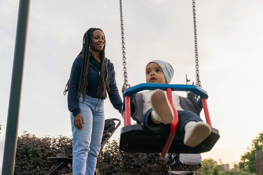 Woman pushing baby on swing in outdoor playground