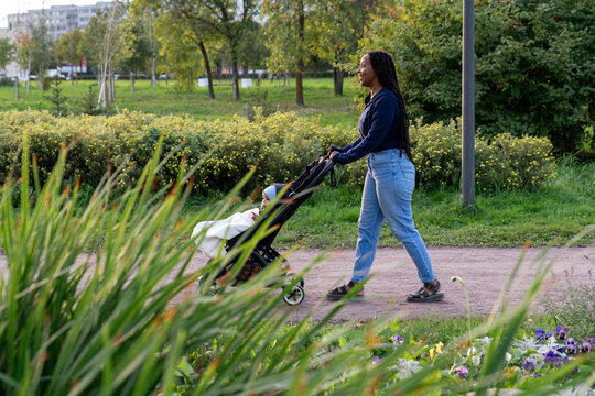 Parent pushing stroller on park path near lake and city buildings