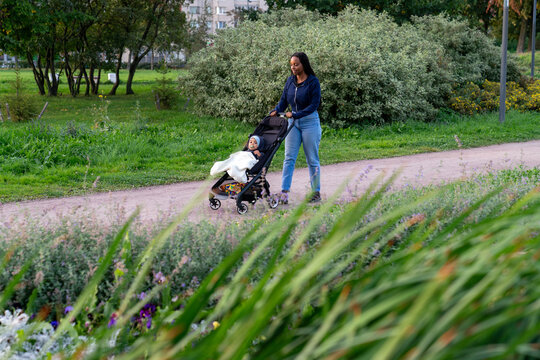Parent pushing baby stroller by lakeside path in city park