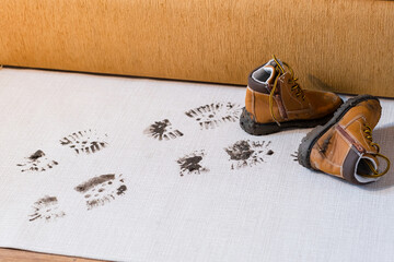 Muddy footprints trail across a clean floor, with a pair of brown boots resting nearby. Dirty...