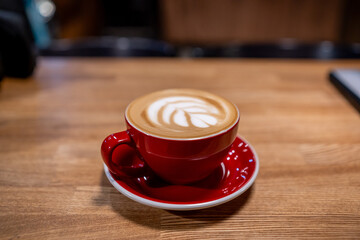 A cup of coffee, a cappuccino in a red mug on a wooden table