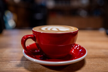 A cup of coffee, a cappuccino in a red mug on a wooden table