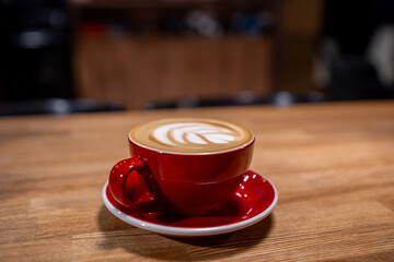 A cup of coffee, a cappuccino in a red mug on a wooden table
