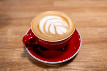 A cup of coffee, a cappuccino in a red mug on a wooden table
