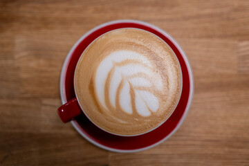 A cup of coffee, a cappuccino in a red mug on a wooden table