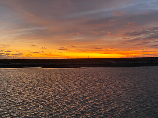 A stunning sunset over a tranquil water body, with vivid orange and yellow hues blending into a dramatic sky, casting reflections on rippling waves.