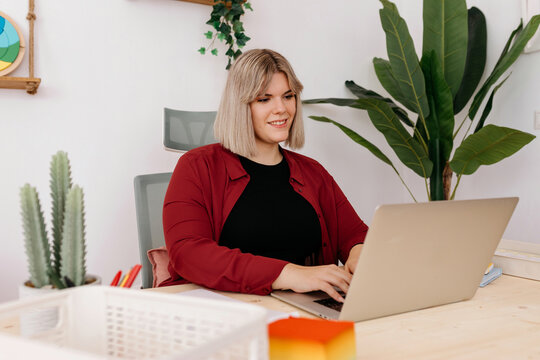 Cheerful curvy lady typing on laptop in office