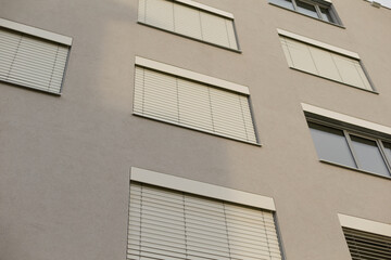 The architectural design features a substantial building that incorporates numerous windows adorned with blinds, enhancing both style and functionality