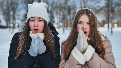 Two young girls warming their hands on a snowy winter day in the park