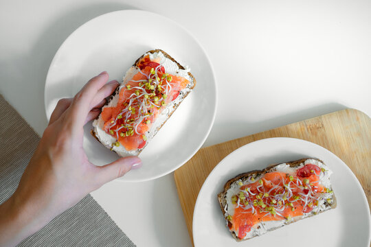 Hand reaching for smoked salmon toast with sprouts and cream cheese
