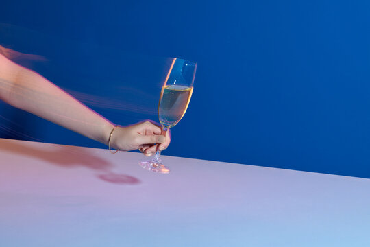 Woman holding glass of champagne on white table over blue background