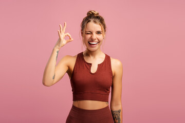 Happy fit woman showing ok or perfect gesture, winking at camera, isolated on pink