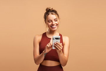 Happy sporty woman chatting on mobile phone, posing in studio isolated on beige background