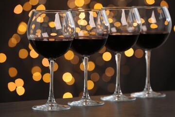 Tasty red wine in glasses on table against dark background with blurred lights, bokeh effect