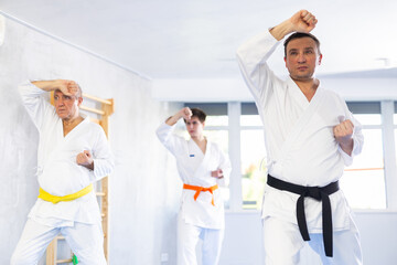 Middle-aged man with other athletes of different ages in kimonos try new fighting techniques at karate lessons