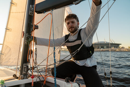 Man Adjusting Sailboat Ropes on Water