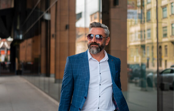 A happy, mature man in elegant, stylish clothes walking through the city street.