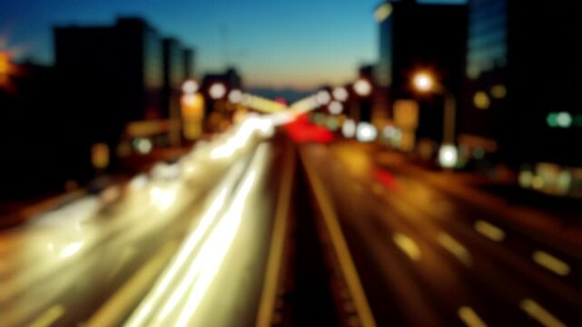 Timelapse: blurred nighttime cityscape with streaking car lights on a busy highway. Long trails against dark urban silhouettes and blue twilight sky.
