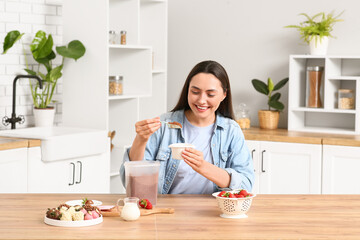 Beautiful young woman preparing chocolate covered strawberries in kitchen