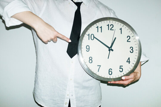 Person wearing office work shirt and tie holding and pointing a clock